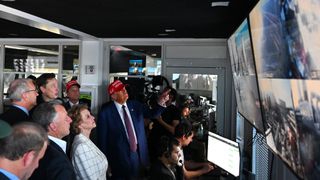 толпа хорошо одетых людей стоит в комнате управления полетами, пока инженеры смотрят на экраны своих компьютеров